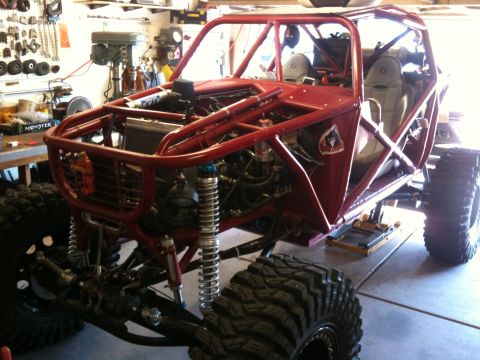 Suzuki Samurai - Three-quarter front view of a dark red tube-chassis rock buggy under assembly in a home garage, with a tube front bumper, exposed radiator,…
