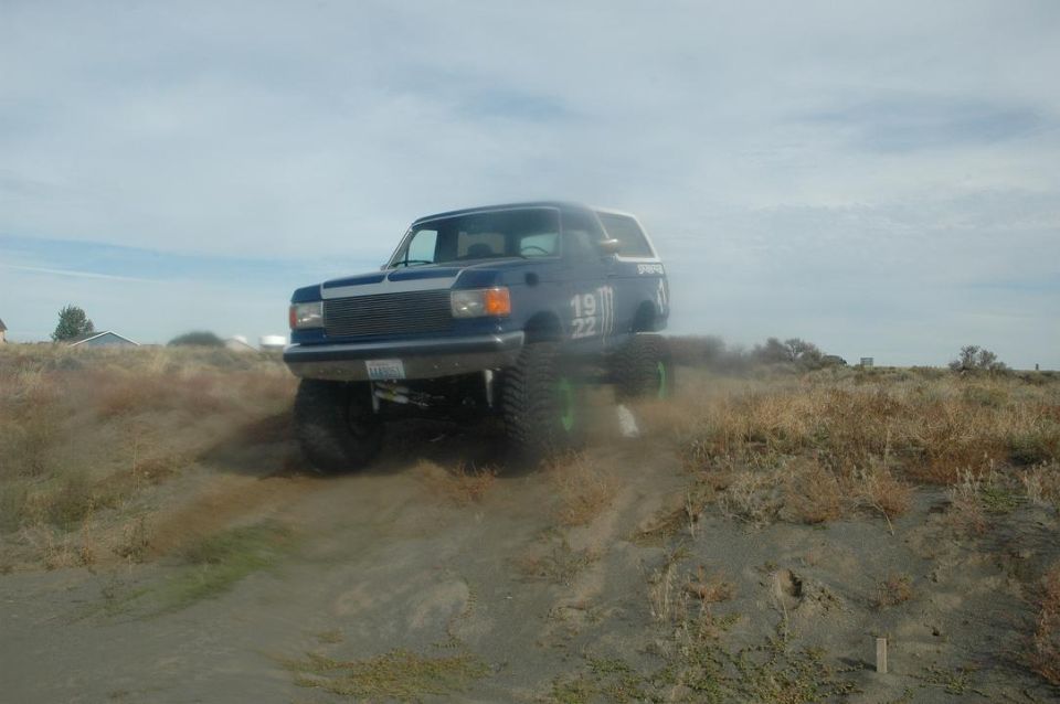 Blue Ford Bronco with custom grille, large tires, and "19 22" graphics on the side, driving on a dirt hill
