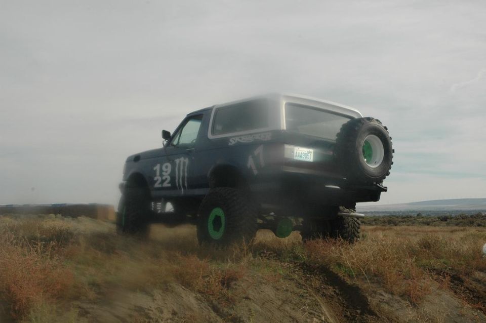 1987 Ford Bronco with "19 22" and Monster Energy logos on the side, driving on a dirt hill