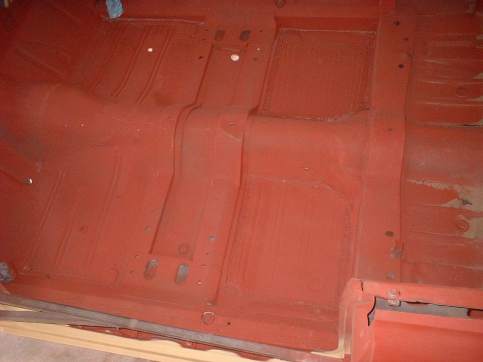 Red painted vehicle floor pan with visible structural ribs and mounting holes