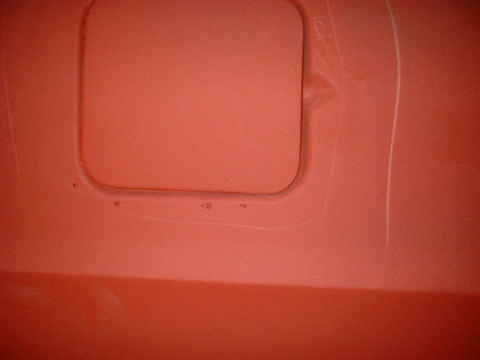 Red car fuel door with visible scuffs and a small dent