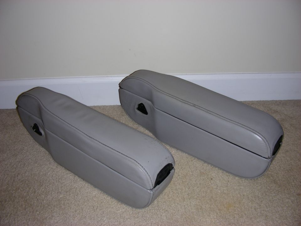Two gray leather arm rests with black latches on a carpeted floor