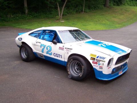1978 Ford Mustang II - A modified Ford Mustang II race car with a roll cage and racing decals is parked on asphalt.