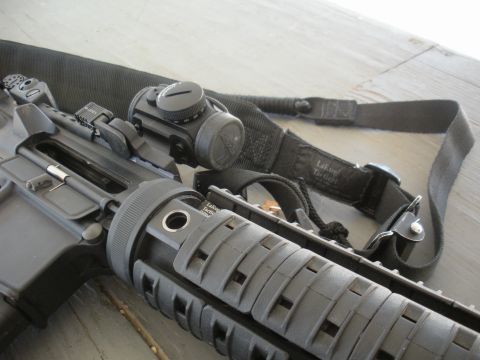 1996 Ford Bronco - A tactical rifle is equipped with a red dot sight and a black sling, resting on a wooden surface.