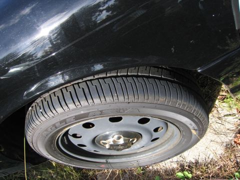 1991 Ford LTD Crown Victoria - Close-up of a black car's fender and wheel, showing a steel rim and tire with visible text.