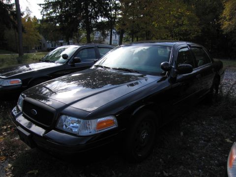 1991 Ford LTD Crown Victoria - Two black sedans are parked outdoors, with the front vehicle in a 3/4 front view.