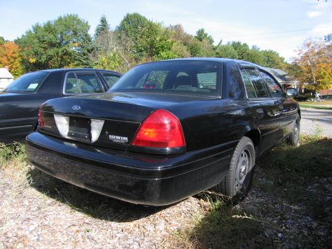 1991 Ford LTD Crown Victoria - A black Ford Crown Victoria is parked next to another vehicle, with trees and a house in the background.