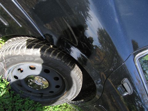 1991 Ford LTD Crown Victoria - Close-up of a black car's rear wheel and body panel, with visible damage.