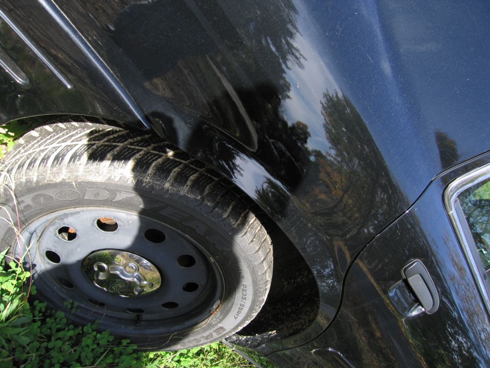 Black car rear wheel and quarter panel, showing a dent near the wheel well