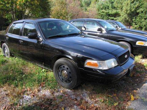 1991 Ford LTD Crown Victoria - Three black Ford Crown Victoria police cars are parked in a grassy area with trees in the background.