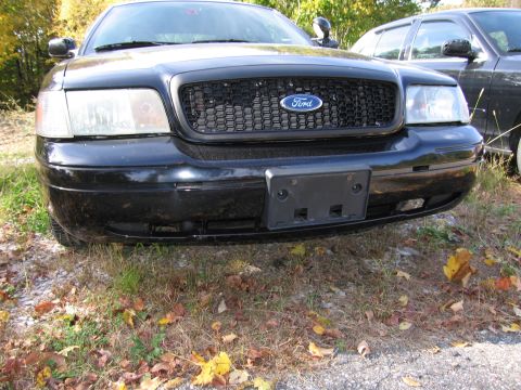 1991 Ford LTD Crown Victoria - A black Ford Crown Victoria is parked in front of another vehicle, with a honeycomb grille and visible headlights.