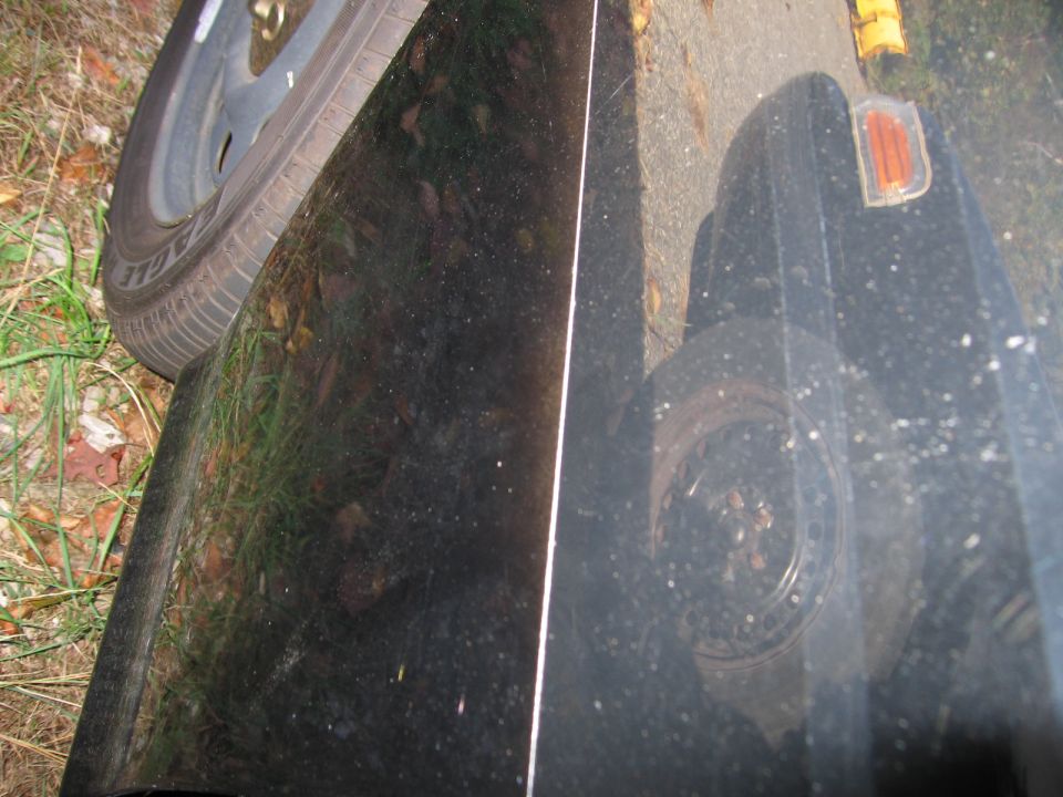 Black car fender with a tire visible on the left; another tire and orange marker light visible on the right