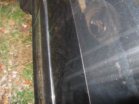 1991 Ford LTD Crown Victoria - The side of a black vehicle is shown, with a portion of the wheel and surrounding grass visible.