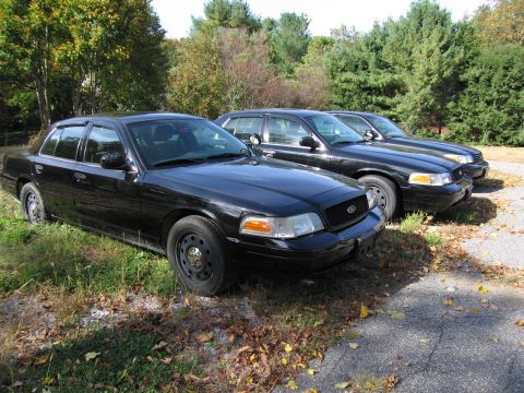 1991 Ford LTD Crown Victoria - Three black Ford Crown Victoria police cars are parked in a line outdoors.