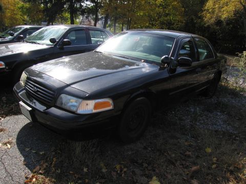 1991 Ford LTD Crown Victoria - A black Ford Crown Victoria sedan is parked in a lot with other vehicles, showing its front quarter profile.