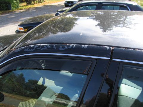 1991 Ford LTD Crown Victoria - A black sedan is parked behind another vehicle, with visible peeling paint on the roof trim.