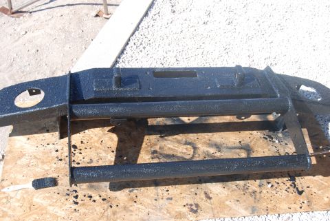 1982 Ford Bronco - A black painted steel bumper with brush guard is shown on plywood, with a brush and paint splatters nearby.