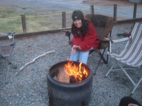 1996 Ford Bronco - A woman enjoys a campfire in a gravel campsite, surrounded by camping chairs and a wooden fence.