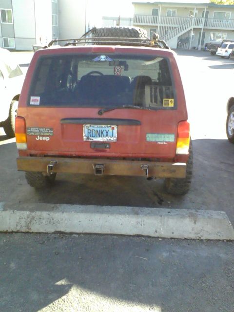 1998 Jeep Cherokee - A red 1998 Jeep Cherokee is parked, showing its rear end with a custom bumper and spare tire on the roof.