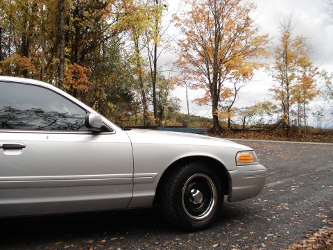 2000 Ford Crown Victoria - A silver 2000 Ford Crown Victoria is seen from the front quarter angle on a road surrounded by fall foliage.