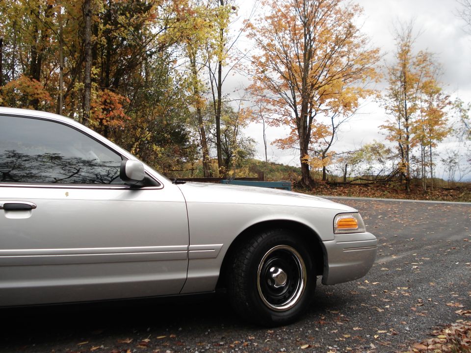 Silver 2000 Ford Crown Victoria, front quarter panel and side visible, parked on a road with autumn trees