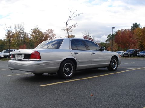 2000 Ford Crown Victoria - A silver sedan is parked in a lot with trees showing fall colors in the background.