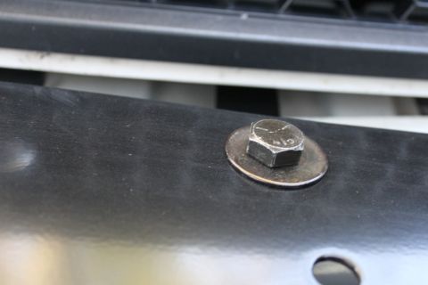 2003 Ford Crown Victoria - A bolt is shown attached to a black surface, with a hint of a grille in the background.