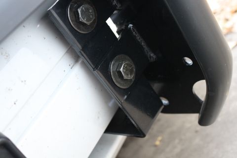 2003 Ford Crown Victoria - A black metal bracket with bolts attaches to a white panel, likely for a vehicle accessory.