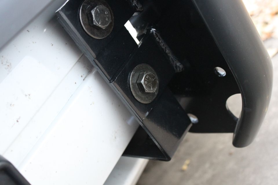 Black steel bracket bolted with hex bolts to white vehicle body