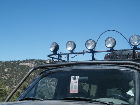 1982 Ford Bronco - A vehicle equipped with a roof rack and multiple spotlights is seen against a clear blue sky and a backdrop of hills.