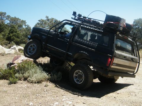 1982 Ford Bronco - Modified black Ford Bronco navigating a rocky trail with its tires on uneven ground.