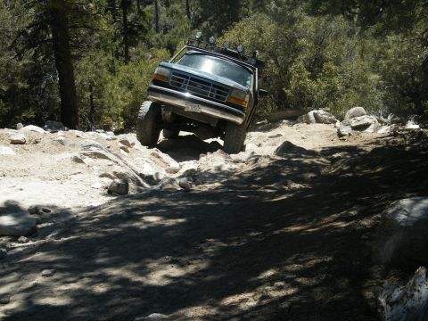 1982 Ford Bronco - This SUV, likely a 1992 Ford Bronco, tackles a challenging rocky trail with its front wheels angled upwards.