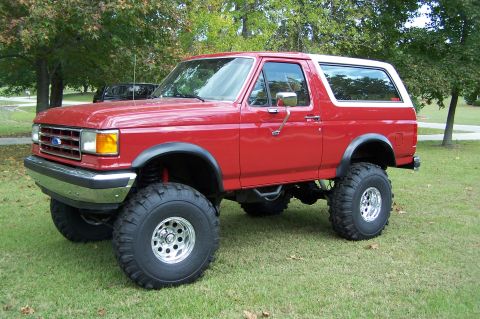 1990 Ford Bronco - This lifted Ford Bronco sits on a grassy area with trees in the background.