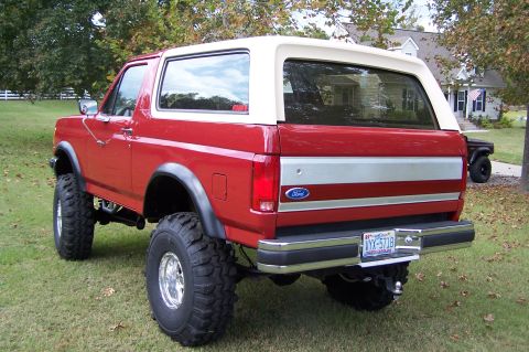 1990 Ford Bronco - This red 1990 Ford Bronco features a white top and is lifted with large tires.