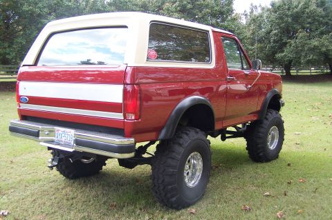 1990 Ford Bronco - Rear view of a red 1990 Ford Bronco with a tan removable top and lifted suspension.