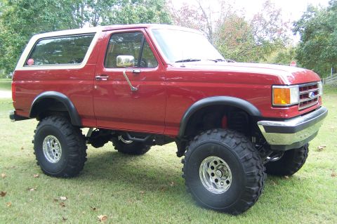 1990 Ford Bronco - Red 1990 Ford Bronco lifted with off-road tires sits on a grassy lawn.
