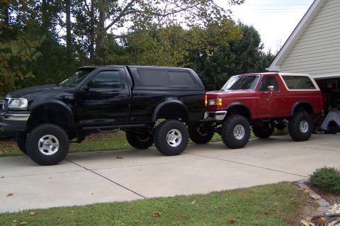 1990 Ford Bronco - Two modified Ford trucks, a Bronco and an F-150, are parked side-by-side in a driveway.