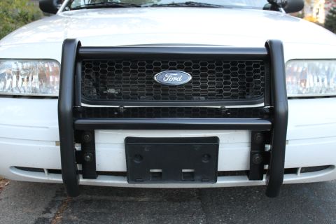 2003 Ford Crown Victoria - The front grille and headlights of a white Ford Crown Victoria are visible behind a black push bar.