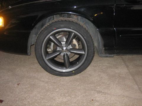 1996 Ford Thunderbird - A close-up shot focuses on the front wheel and fender of a black vehicle, revealing its tire and rim details.