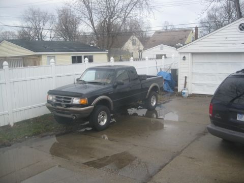 1995 Ford Ranger - A black 1995 Ford Ranger pickup truck is parked in a driveway with puddles, next to a white fence and garage.