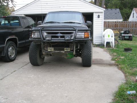 1995 Ford Ranger - A black Ford Ranger with a modified front bumper and large tires is parked in front of a garage.