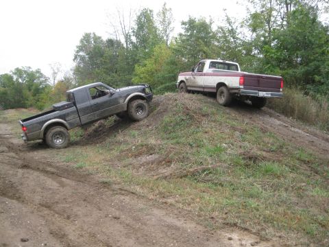 1995 Ford Ranger - Two pickup trucks navigate a muddy, grassy incline during an off-road excursion.