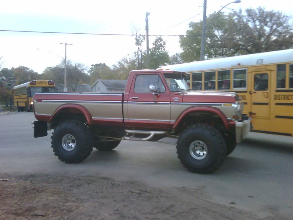 Lifted red and tan pickup truck next to a yellow school bus