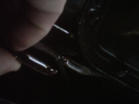 1995 Ford Bronco - Very dark, tight close-up of a hand pointing at a stamped seam or crease line in black-painted sheet metal, with a bright reflected highlig…