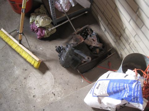 1979 Ford Bronco - A steering gear box sits on a concrete floor next to cleaning supplies and other items.