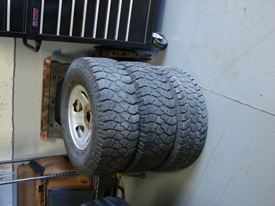 Three off-road tires mounted on silver rims, stacked horizontally