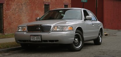 2000 Ford Crown Victoria - This silver 2000 Ford Crown Victoria is parked on a street with brick buildings in the background.