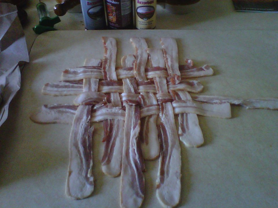 Woven raw bacon strips on a cutting board with spice containers in the background