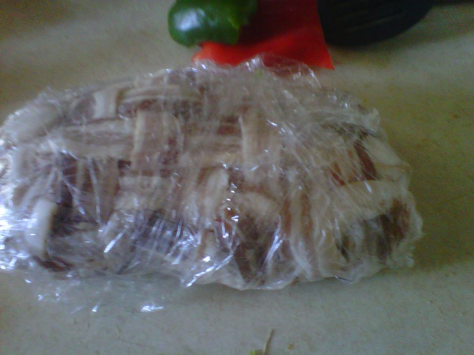 Food wrapped in plastic on a counter, with a green pepper and red pepper visible