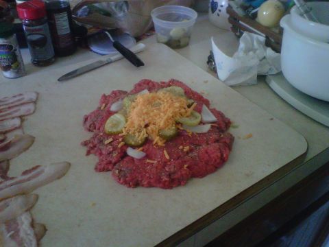 1986 Ford Bronco - A raw hamburger patty is prepared with toppings on a cutting board, with bacon strips to the side.